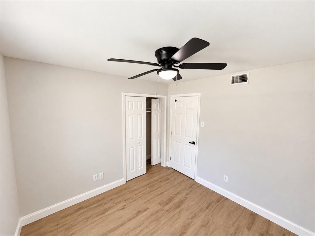 Room featuring wood-finish flooring, a matte black ceiling fan with an integrated light fixture, and six-panel interior doors