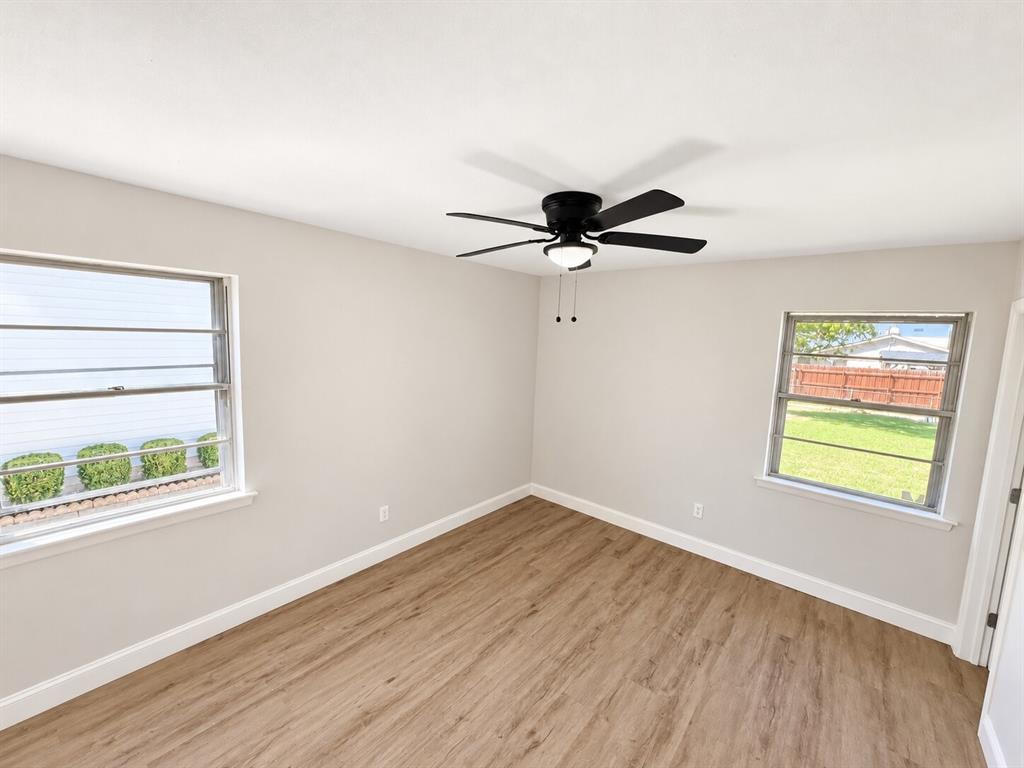 Neutral wall tones paired with wood-finish flooring, dual windows with exterior window bars, and a matte black ceiling fan with an integrated light fixture