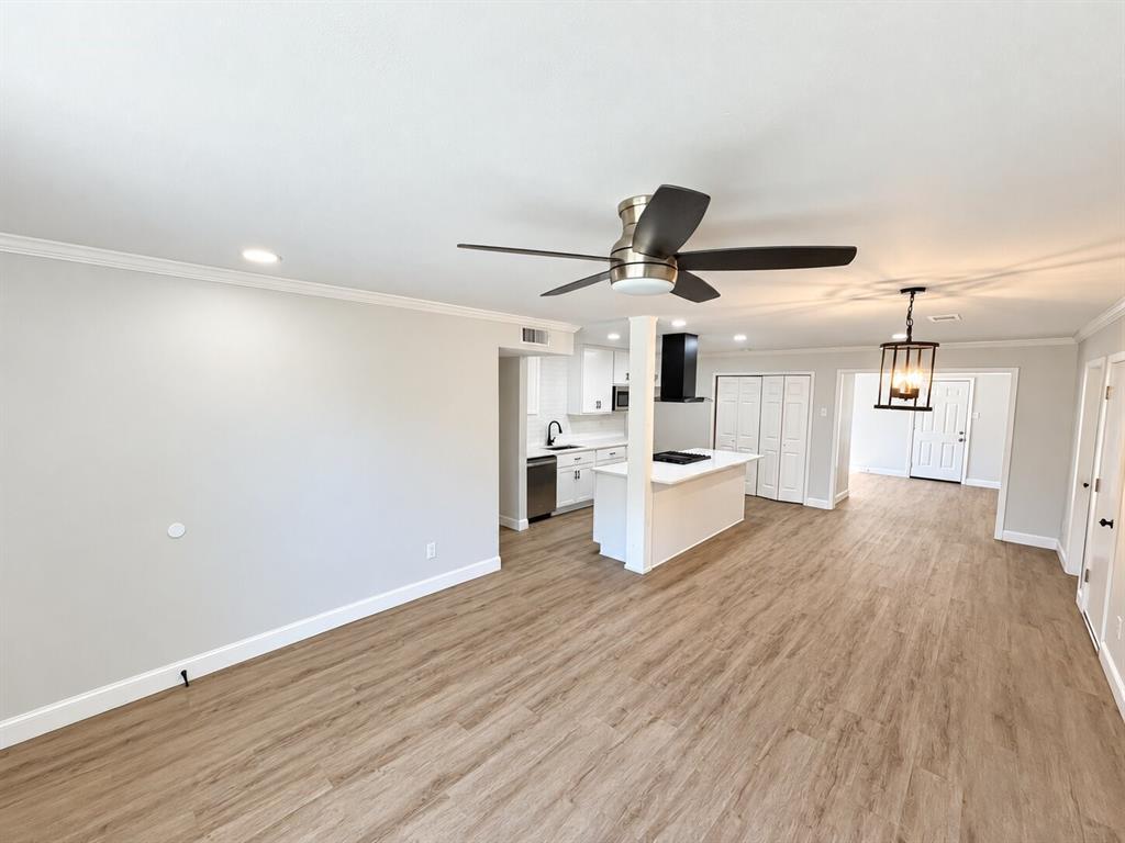 Open-concept interior featuring wood-finish flooring, a kitchen island with stone-finish countertops, recessed lighting, a modern metal-frame pendant light, and a ceiling fan Open-concept interior featuring wood-finish flooring, a kitchen island with stone-finish countertops, recessed lighting, a modern metal-frame pendant light, and a ceiling fan