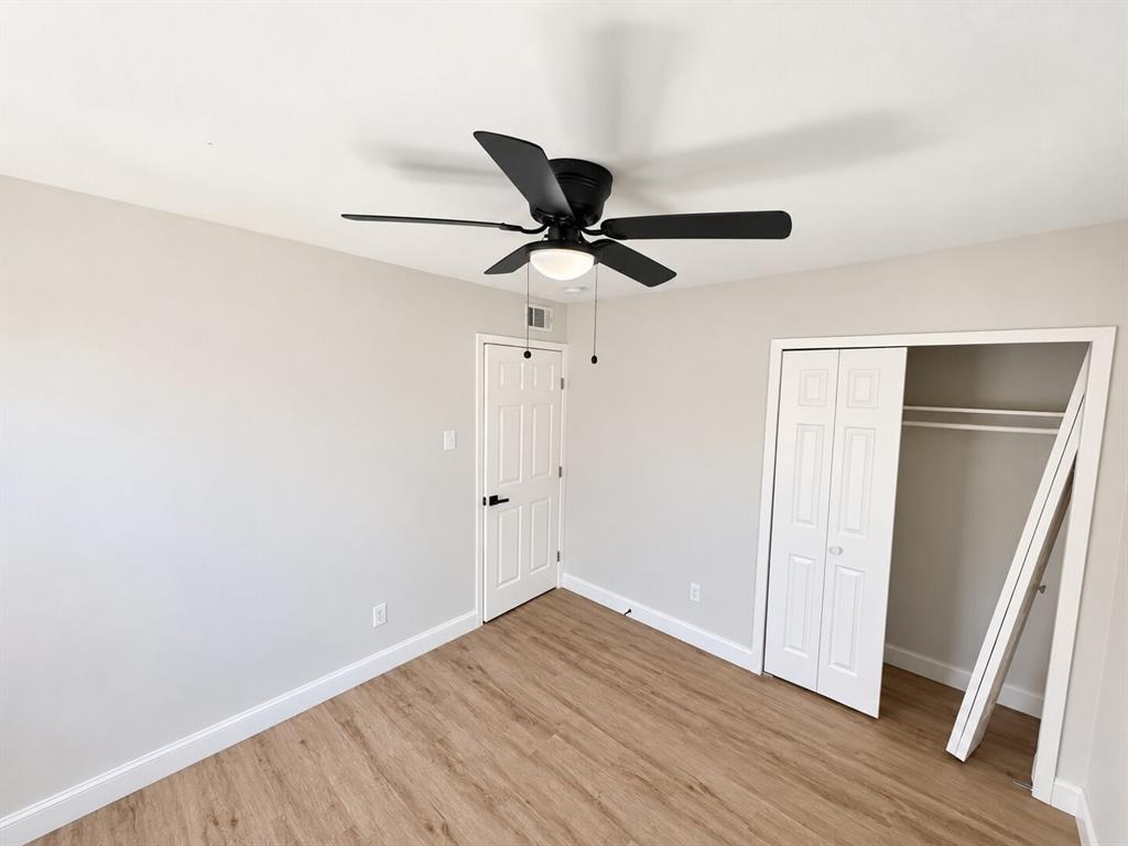Interior room featuring wood-finish flooring, a ceiling fan with integrated light fixture, a paneled interior door with matte black hardware, and a closet with bifold doors