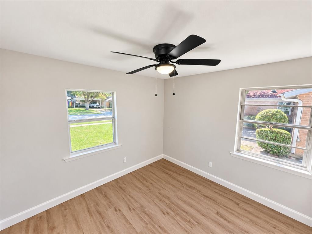 Interior space featuring wood-finish flooring, neutral wall paint, two dual-pane windows, and a matte black ceiling fan with integrated lighting