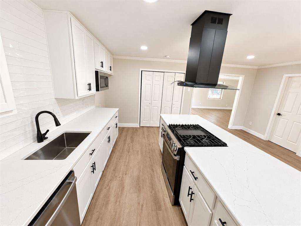 Kitchen featuring white cabinetry, solid-surface countertops, a center island with an integrated gas cooktop, a stainless steel range, and a ceiling-mounted range hood Kitchen featuring white cabinetry, solid-surface countertops, a center island with an integrated gas cooktop, a stainless steel range, and a ceiling-mounted range hood