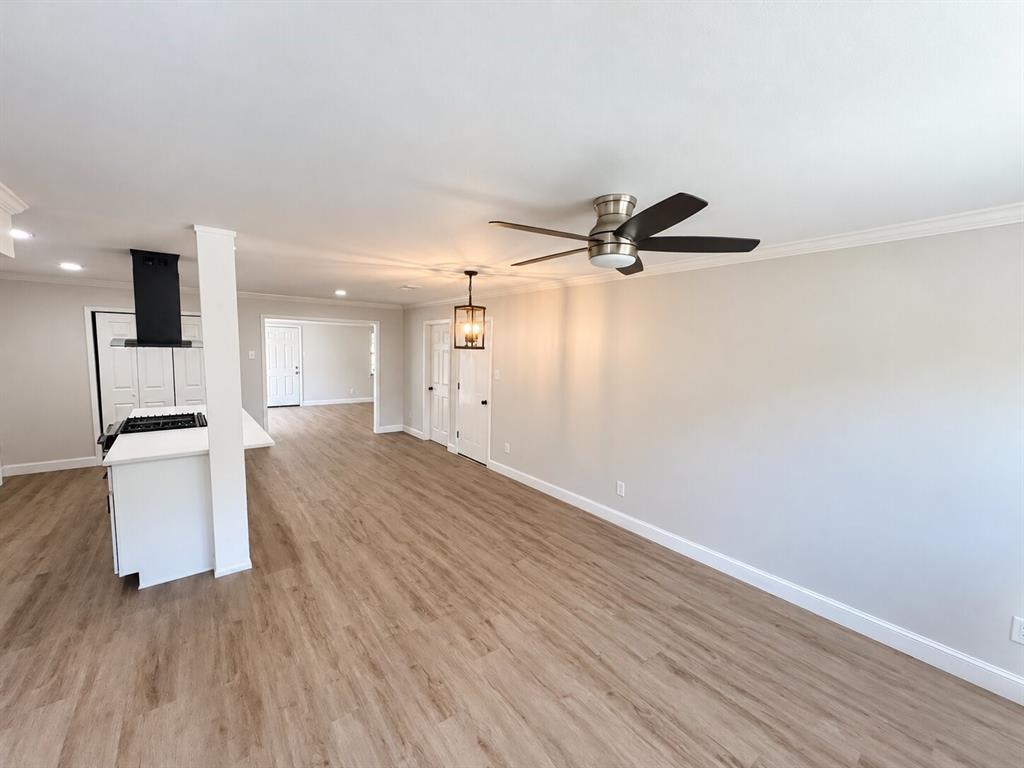 Interior space featuring wood-finish flooring, a matte black range hood, a kitchen peninsula with a white countertop, a ceiling fan, and a metal-framed pendant light fixture Interior space featuring wood-finish flooring, a matte black range hood, a kitchen peninsula with a white countertop, a ceiling fan, and a metal-framed pendant light fixture