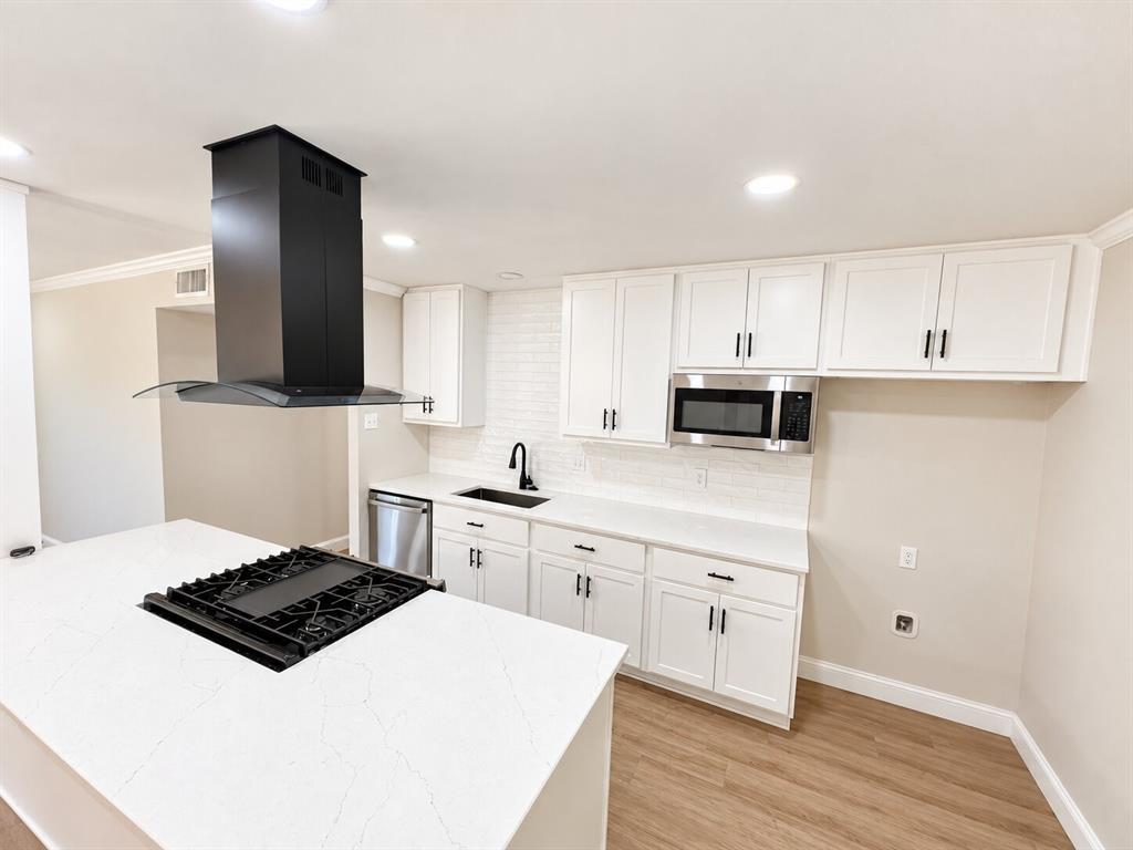 Kitchen featuring a central island with a built-in gas cooktop, quartz countertops, white cabinetry, matte black fixtures, and wood-finish flooring Kitchen featuring a central island with a built-in gas cooktop, quartz countertops, white cabinetry, matte black fixtures, and wood-finish flooring