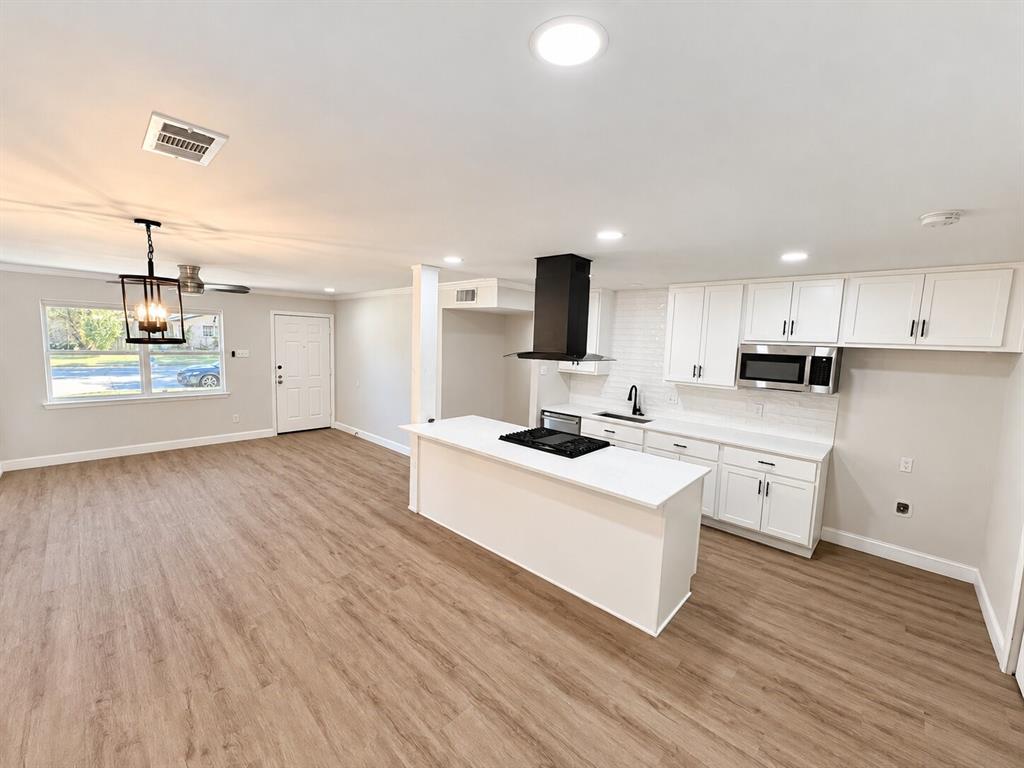 Kitchen featuring white cabinetry, an island with an integrated cooktop, a black range hood, recessed lighting, and wood-finish flooring Kitchen featuring white cabinetry, an island with an integrated cooktop, a black range hood, recessed lighting, and wood-finish flooring