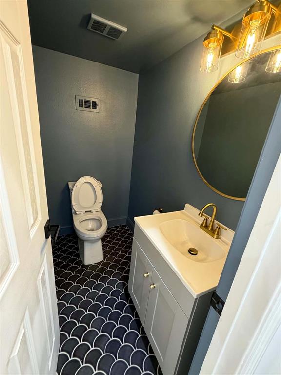 Powder room  featuring patterned scalloped floor tile, vanity with integrated basin, brass-finish faucet and hardware, round gold-framed mirror, and multi-bulb wall lighting