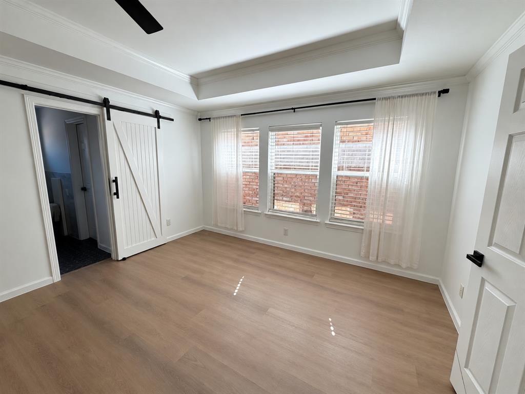 Tray ceiling with recessed lighting, wood-finish flooring, sliding white barn door with matte black hardware, and three-pane window configuration