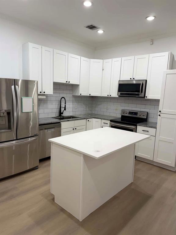 Kitchen featuring white shaker-style cabinetry, stone countertops, a subway tile backsplash, stainless steel appliances, and wood-finish flooring