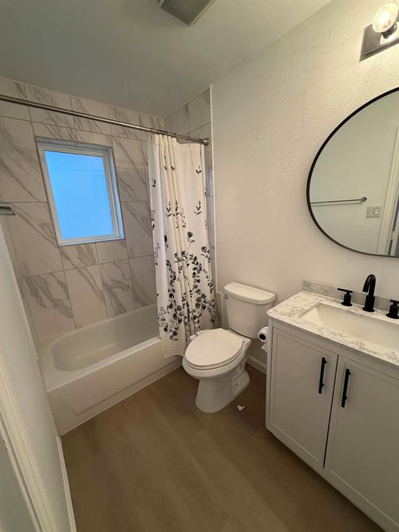 2nd Bathroom featuring a vanity with a stone-finish countertop, undermount sink, and matte black hardware, paired with a shower-tub combination featuring floor-to-ceiling stone-patterned wall tile and a circular vanity mirror