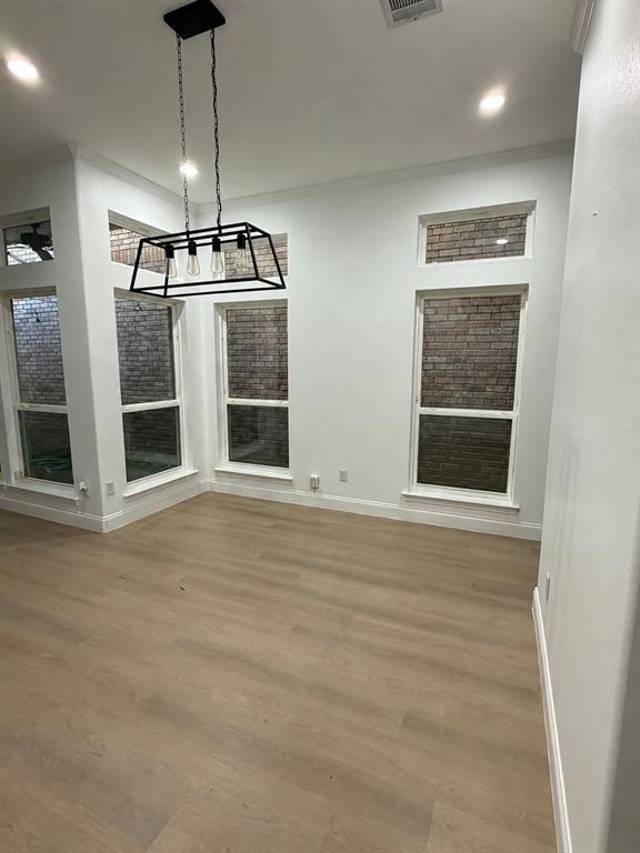 Open-concept space featuring wood-finish flooring, rectangular windows with brick exterior detailing, recessed lighting, and a linear pendant fixture with a matte black frame