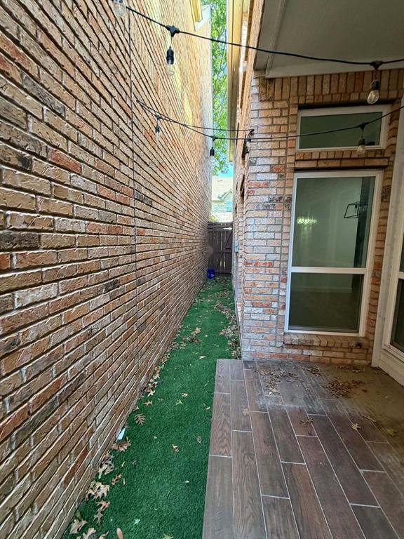 Exterior space featuring brick siding, a paved patio with wood-finish tile, and a synthetic turf side yard