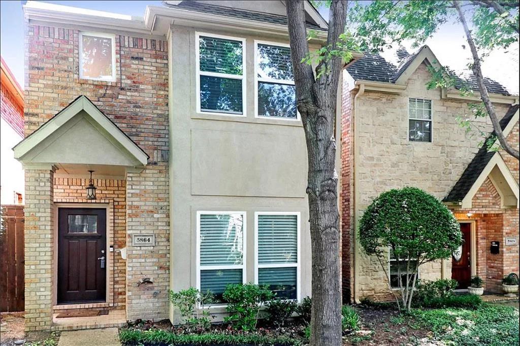 Two-story exterior featuring a mix of brick and stucco siding, a covered entryway with a gabled roofline, dark-finish wooden front door, and multi-pane windows