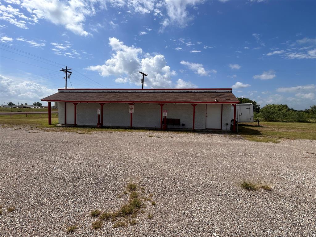 Single-story structure featuring a covered front porch, red-trimmed architectural accents, gravel lot, and multiple exterior access points