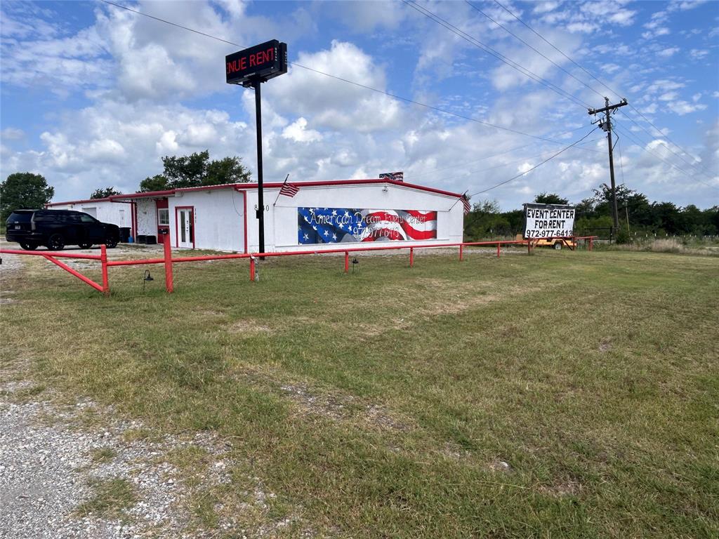 Single-story commercial building featuring a metal facade, gravel parking area, expansive open grounds, and a pole-mounted signage structure Single-story commercial building featuring a metal facade, gravel parking area, expansive open grounds, and a pole-mounted signage structure