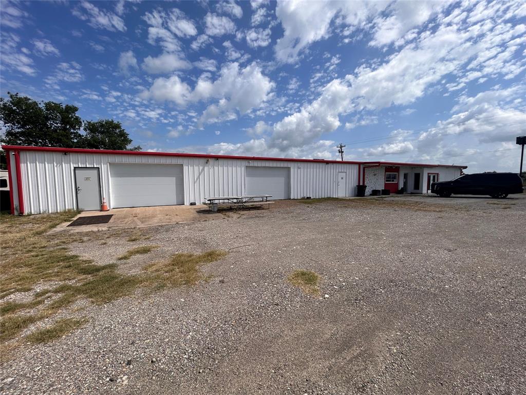 Metal-sided exterior building featuring two overhead garage doors, multiple exterior entry points, and a spacious gravel lot Metal-sided exterior building featuring two overhead garage doors, multiple exterior entry points, and a spacious gravel lot