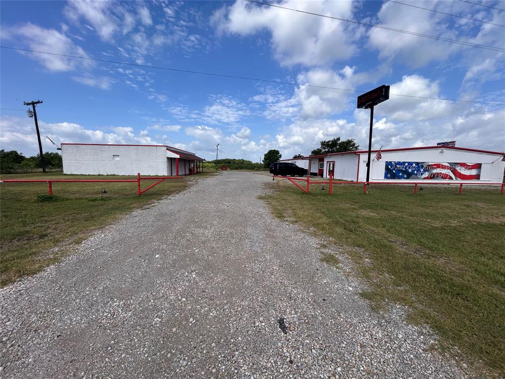 Commercial property featuring two exterior structures, expansive gravel grounds, and red metal perimeter fencing Commercial property featuring two exterior structures, expansive gravel grounds, and red metal perimeter fencing
