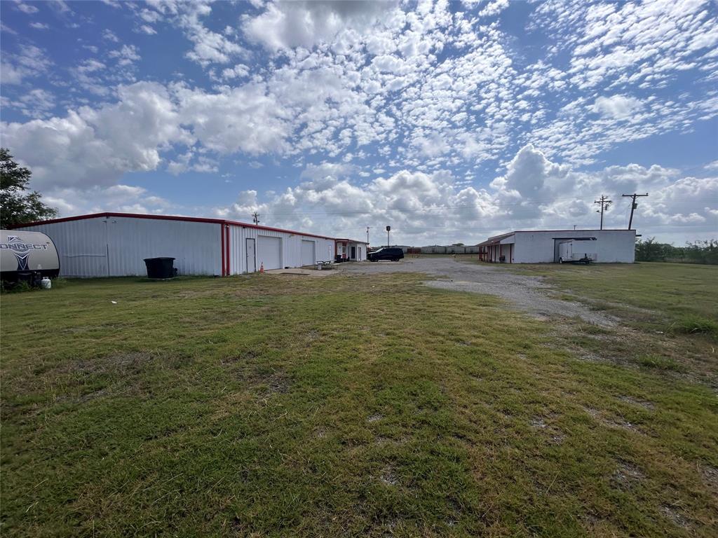 Expansive lot featuring two metal-sided warehouse buildings, multiple roll-up garage doors, and a gravel parking area