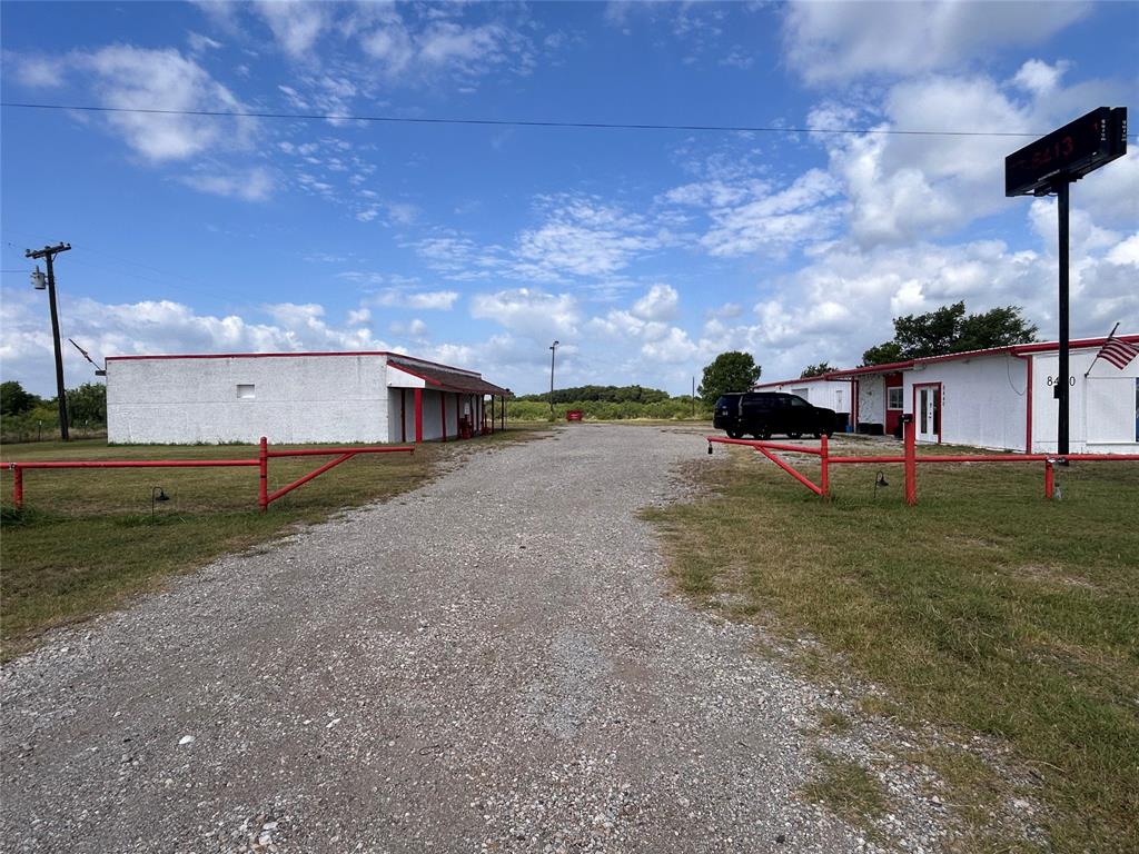 Exterior of commercial structures featuring white masonry construction with red trim, a gravel surface, and red metal access gates