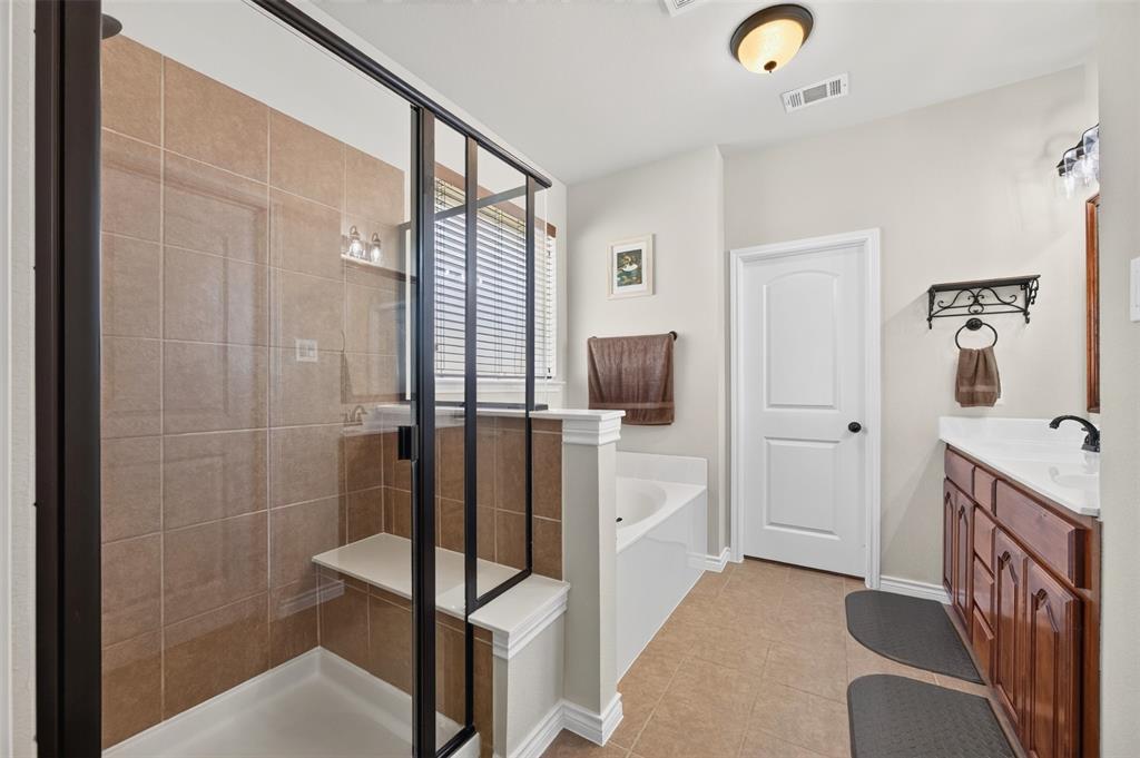 Walk-in shower featuring a built-in bench, tiled surround, and a dark-finish frame, paired with a white soaking tub, wood-finish cabinetry, and a countertop with an integrated sink