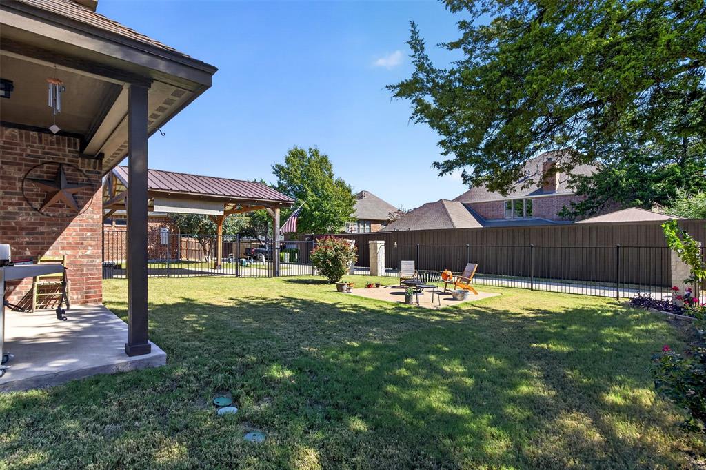 Backyard featuring a covered brick patio, metal-roofed pavilion, stone-paver hardscaping, manicured lawn, and full-perimeter fencing