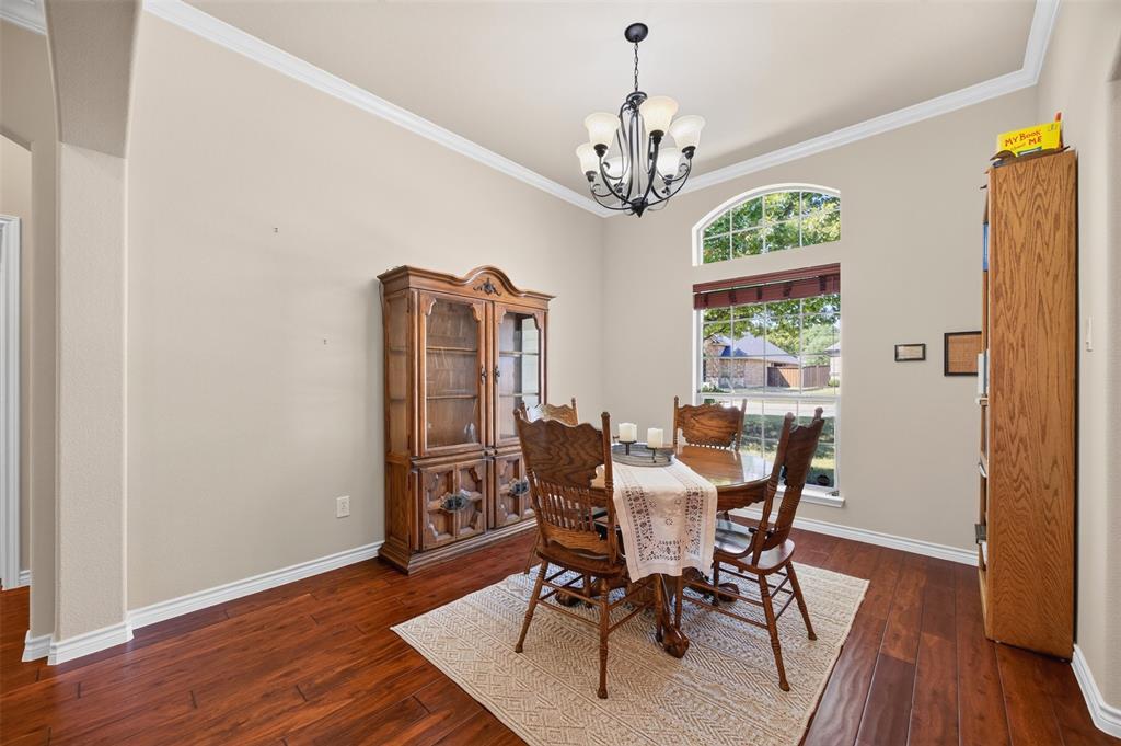 Dining area featuring wood-finish flooring, an arched window, crown molding, and a tiered multi-light chandelier