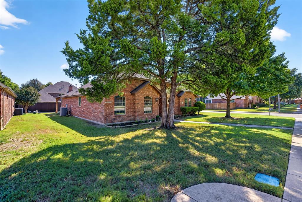 Brick exterior featuring arched windows, mature canopy trees, and a manicured lawn
