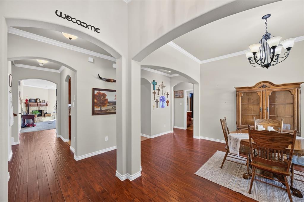 Arched architectural detailing, wood-finish flooring, and crown molding throughout, illuminated by a multi-arm chandelier and recessed lighting