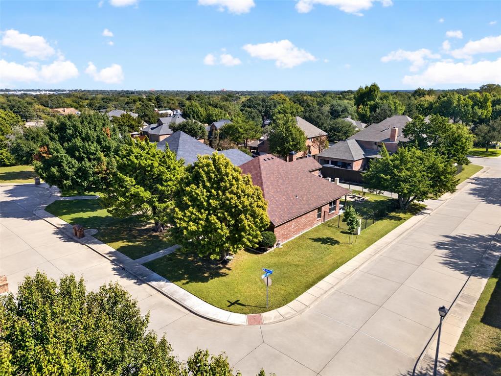 Corner lot featuring a brick exterior, hipped roofline, mature trees, and concrete sidewalk infrastructure