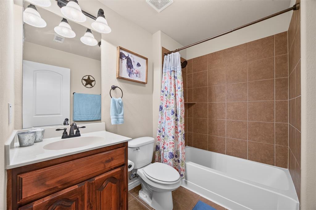 Bathroom featuring a wood-finish vanity with an integrated basin, matte black faucet, wall-mounted light fixture, and a tub-shower combination with ceramic tile surround