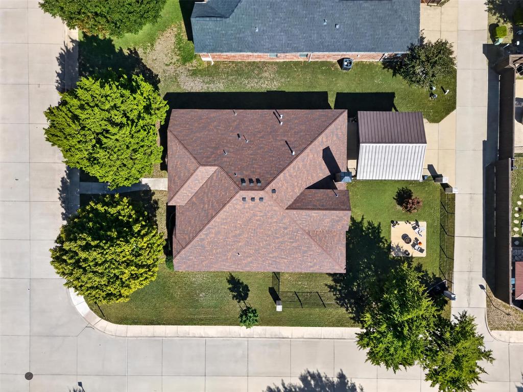 Aerial view featuring a shingle roof, a detached metal-roofed structure, and mature trees on a corner lot