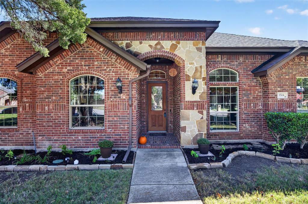 Brick exterior featuring stone masonry detailing, arched window accents, wood-finish entry door with glass insert, and tiered landscaping beds