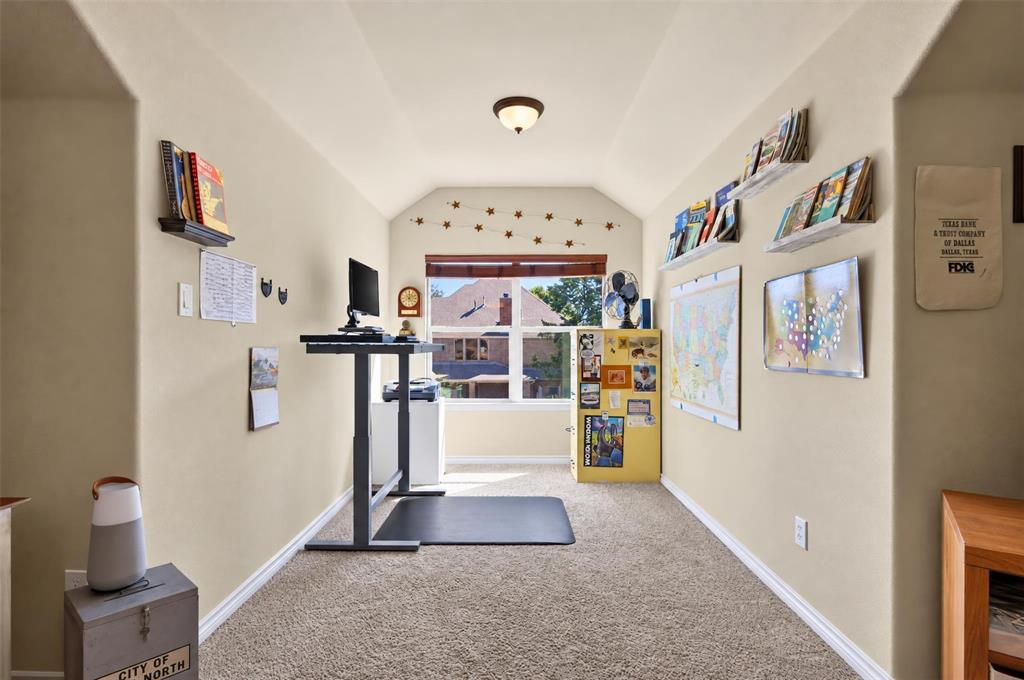 Vaulted ceiling with integrated flush-mount lighting, carpeted flooring, and a window providing natural light