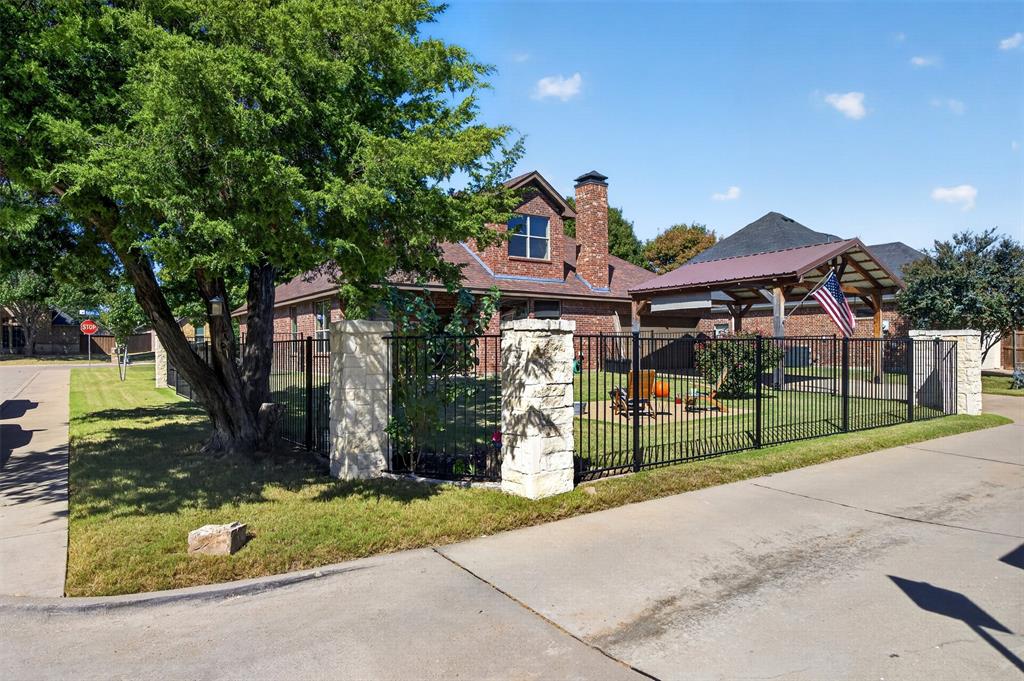 Brick exterior featuring a multi-tiered roofline, stone-pillar metal fencing, and a detached covered pavilion