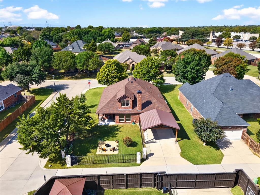 Aerial view of brick exterior home featuring a steep-pitched roof, covered carport, dormer window, and fenced yard with a stone-surfaced patio area