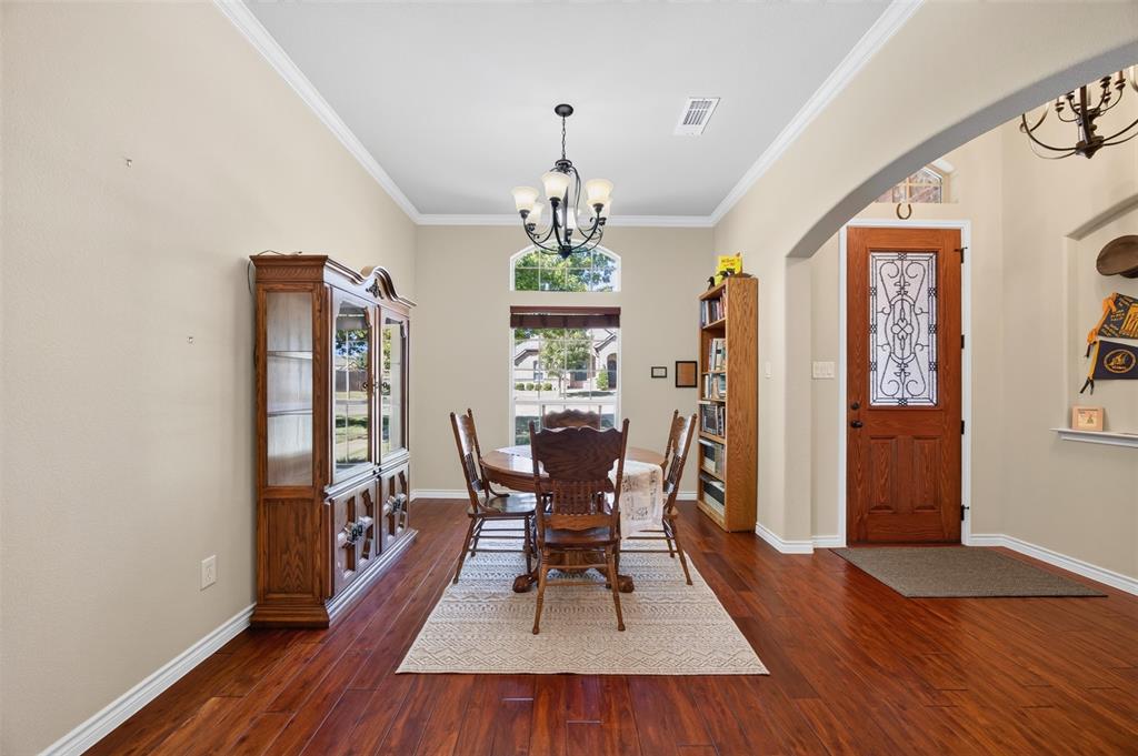 Dining area featuring wood-finish flooring, crown molding, a central chandelier, and an arched window with transom detailing