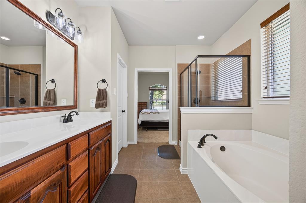 Bathroom featuring a wood-tone vanity with a solid-surface countertop, soaking tub, glass-enclosed shower, and neutral tile flooring