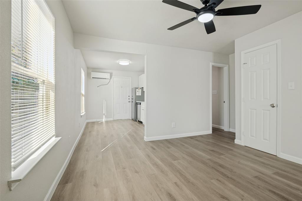 Wood-finish flooring, matte black ceiling fan with integrated lighting, wall-mounted ductless air conditioning unit, and white six-panel interior doors Wood-finish flooring, matte black ceiling fan with integrated lighting, wall-mounted ductless air conditioning unit, and white six-panel interior doors