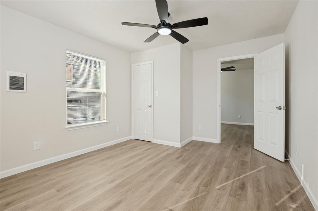 Neutral-toned room featuring wood-finish flooring, a ceiling fan with integrated lighting, and a six-panel door Neutral-toned room featuring wood-finish flooring, a ceiling fan with integrated lighting, and a six-panel door
