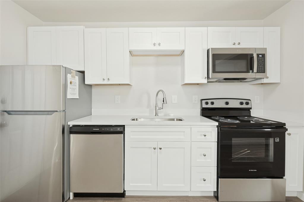 Kitchen featuring white shaker-style cabinetry, solid-surface countertops, stainless steel appliances, and a gooseneck faucet Kitchen featuring white shaker-style cabinetry, solid-surface countertops, stainless steel appliances, and a gooseneck faucet