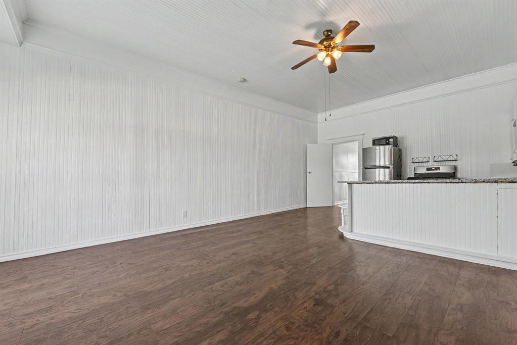 Beadboard wall paneling, wood-finish flooring, white beadboard ceiling, ceiling fan with integrated lighting, and kitchen peninsula with stone-finish countertop