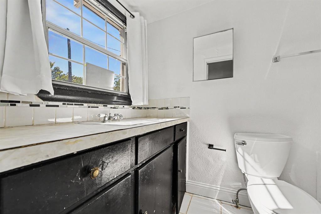 Vanity featuring stone-surfaced countertop, integrated basin, and dark-finished cabinetry, accented by multi-toned mosaic tile backsplash, rectangular wall-mounted mirror, and tile flooring