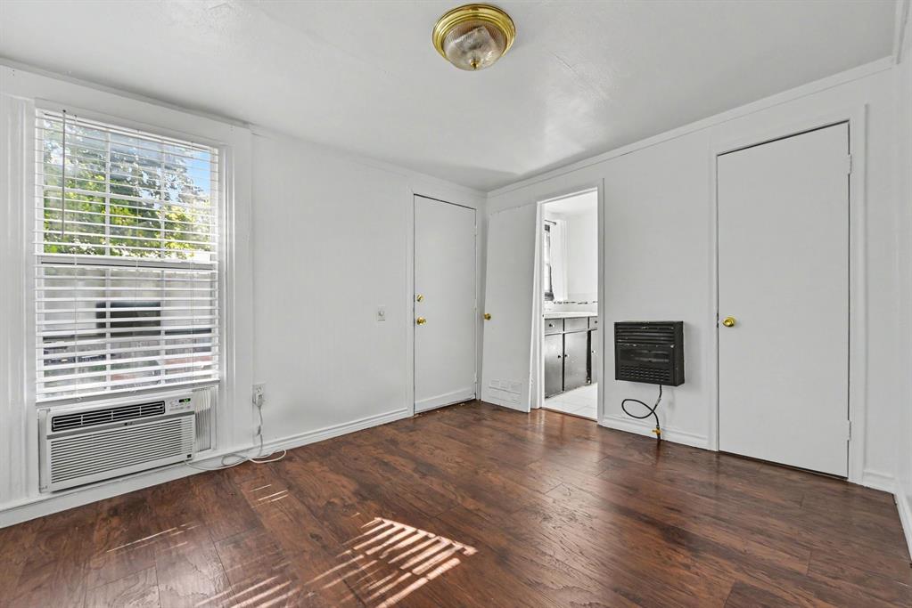 Interior space featuring wood-finish flooring, a window with integrated blinds, wall-mounted heating unit, and flush-mount ceiling lighting