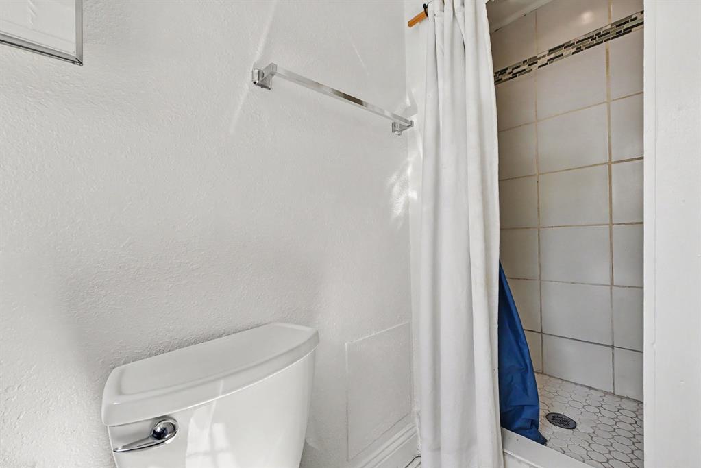 Bathroom featuring a white ceramic toilet, chrome towel bar, walk-in shower with square wall tile, mosaic floor tiling, and a decorative tile accent border