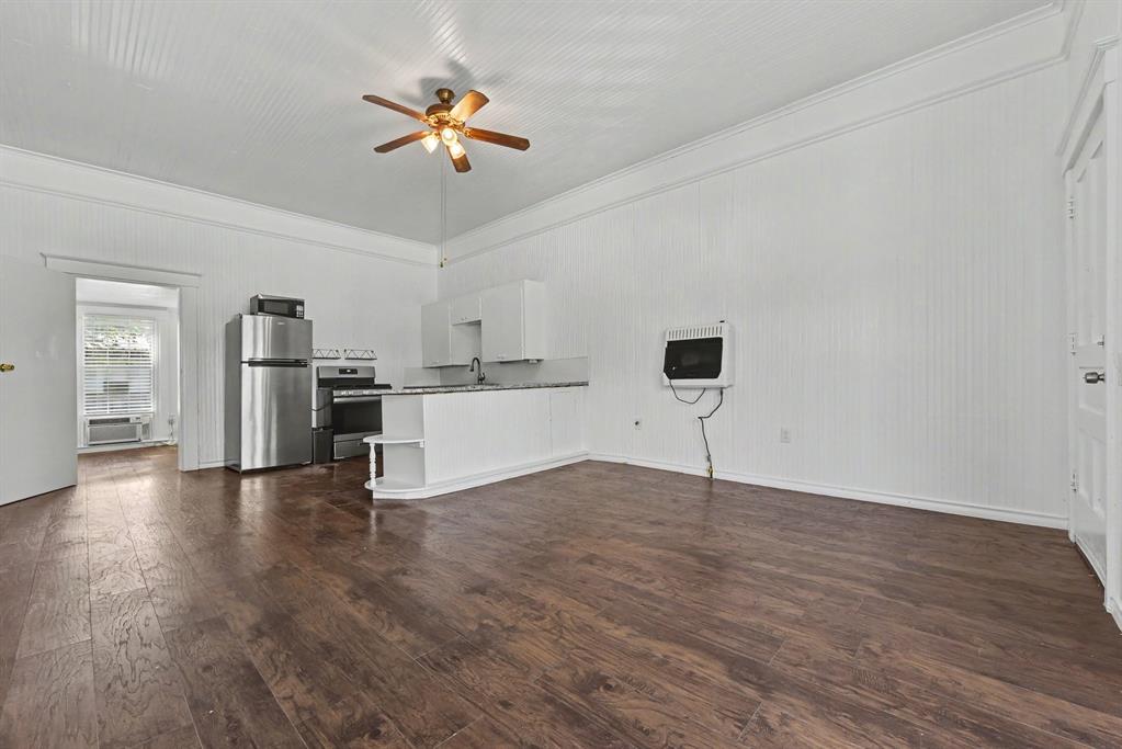 Interior featuring beadboard walls, wood-finish flooring, high ceilings, a ceiling fan, and a kitchen with white cabinetry and a breakfast bar