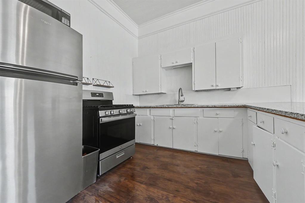 Kitchen featuring stainless steel appliances, wood-finish flooring, white cabinetry, beadboard wall paneling, and stone-surfaced countertops