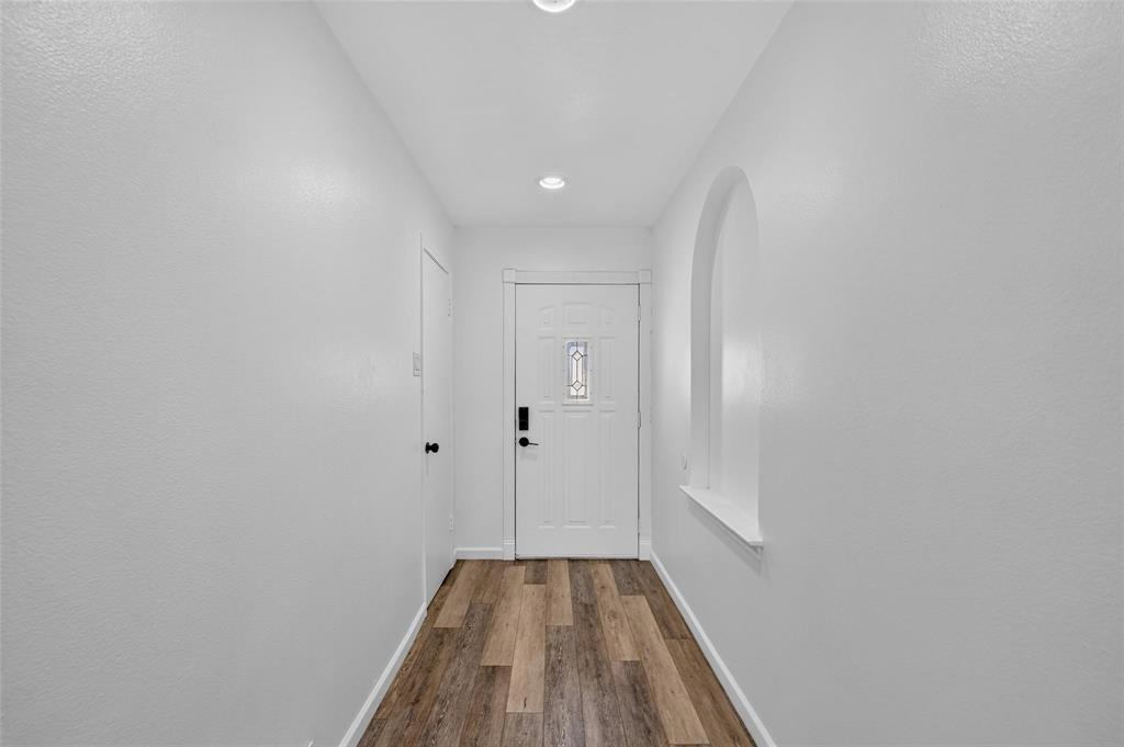 Entryway featuring wood-finish flooring, a white paneled front door with a glass insert, recessed lighting, and a recessed wall niche with an arched top