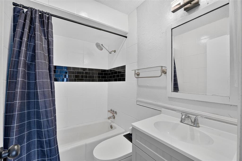 Bathroom featuring a vanity with a white countertop and integrated basin, a combination tub and shower with a high-contrast black tile inlay, and a framed wall mirror