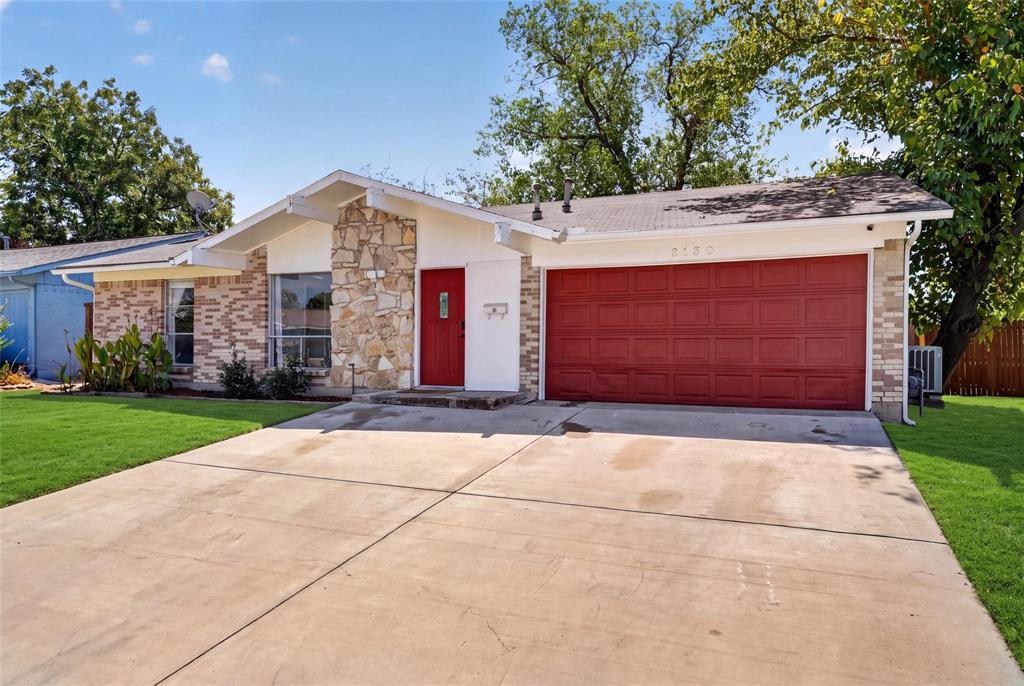 Mid-century ranch exterior featuring a stone facade, low-pitched roofline, attached two-car garage, and concrete driveway Mid-century ranch exterior featuring a stone facade, low-pitched roofline, attached two-car garage, and concrete driveway