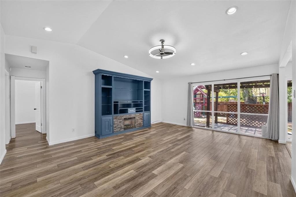 Living area featuring wood-finish flooring, vaulted ceilings, recessed lighting, a built-in media cabinet with a stone-surround electric fireplace, and large glass pane doors Living area featuring wood-finish flooring, vaulted ceilings, recessed lighting, a built-in media cabinet with a stone-surround electric fireplace, and large glass pane doors