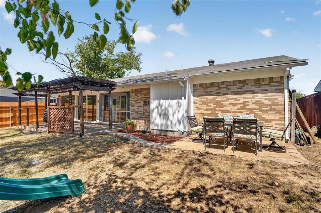Rear exterior featuring a brick and panel facade, a wooden pergola, a concrete patio, and a wood privacy fence